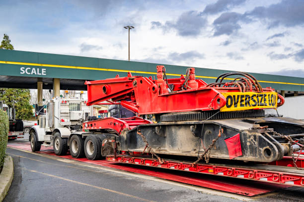 Industrial grade white big rig semi truck carry oversize load on the step deck low profile heavy duty semi trailer going to the scale for weighing the load on the axles for safe driving on highways