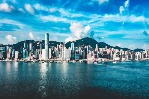 Vibrant hong kong skyline reflecting in the calm harbor under a bright blue sky with scattered clouds