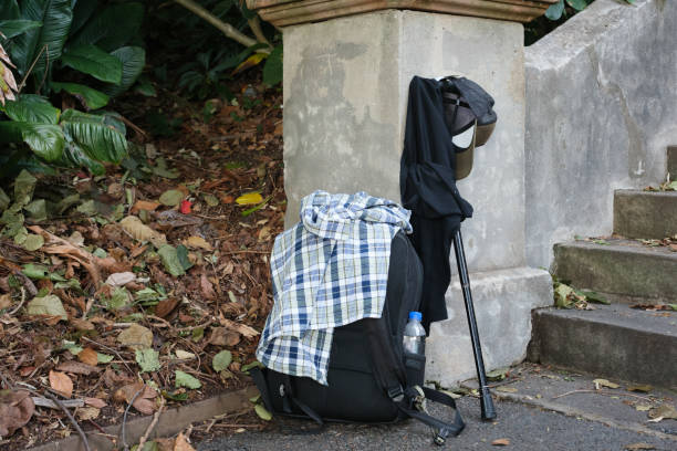 Backpack, clothing and walking stick against a wall in a public park.