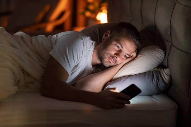istock A sleepless man lying in dark bedroom with mobile phone in hands and scrolling endlessly. 2196286093