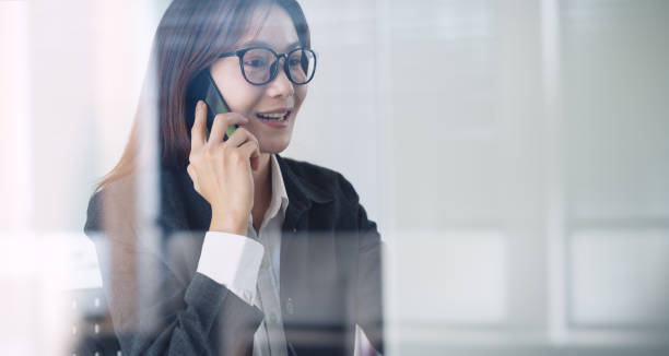 istock Talking on mobile phone. Close up, smiling asian business woman with eyeglasses using mobile phone, talking to customer during working at office, talking on phone solving business issues 2196307656