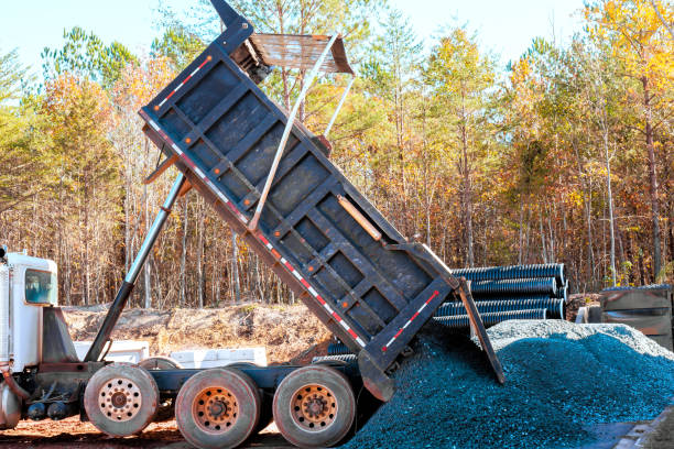 istock Dump truck unloading gravel at a construction site surrounded by autumn trees in bright daylight hours 2196308557