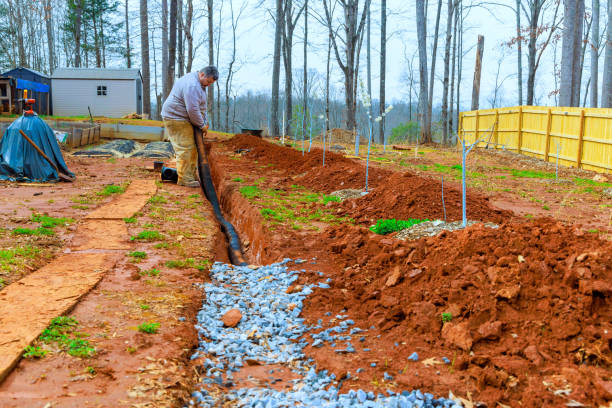 Man digging a trench for landscaping in a rural area with trees in the background during early spring Contractor is digging trench for enhance water flow management, during installing drainage system in backyard flood preparation stock pictures, royalty-free photos & images