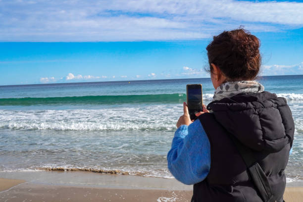 woman photographs the aquatic horizon, on a beach, a day with calm sea and blue sky