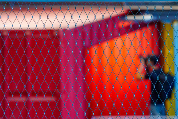 View of warehouse building with closeup of a fence grid, and colorful shipping containers in the background