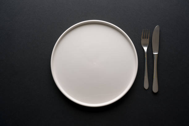 istock Top view of empty ceramic white plate and cutlery on black background 2196324818