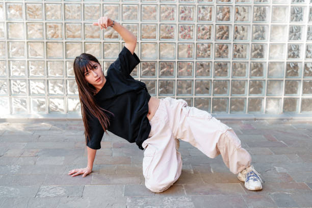 istock Young dancer performs dynamic moves against a glass block wall in urban setting during bright daylight 2196326488