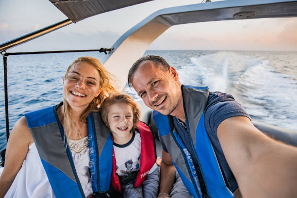 Happy family taking a selfie on a boat at sea. Happy family having fun while taking a selfie during boat ride at sea and looking at camera. yacht selfie stock pictures, royalty-free photos & images