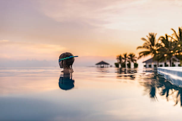 Cute little boy with swimming goggles in the infinity pool at sunset. Copy space.