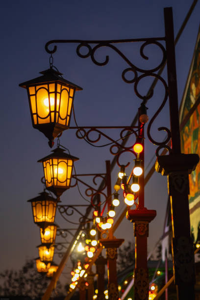 A row of elegant, old-fashioned lanterns hangs from ornate metalwork, casting a warm glow against the twilight sky. Fairy lights add to the magical ambiance. The scene suggests a festive or romantic atmosphere.