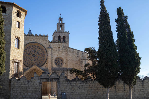 Ancient stone monastery with a large rose window, framed by tall cypress trees under a clear blue sky.  A glimpse of peaceful serenity.
