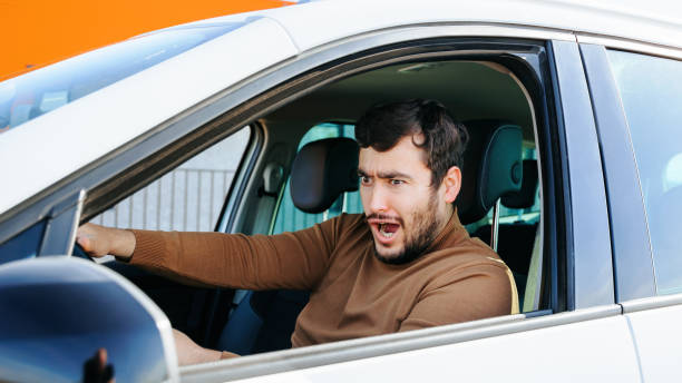 istock Front view a young man sits in a car looking somewhere, grimacing in horror and indignation. 2196348670