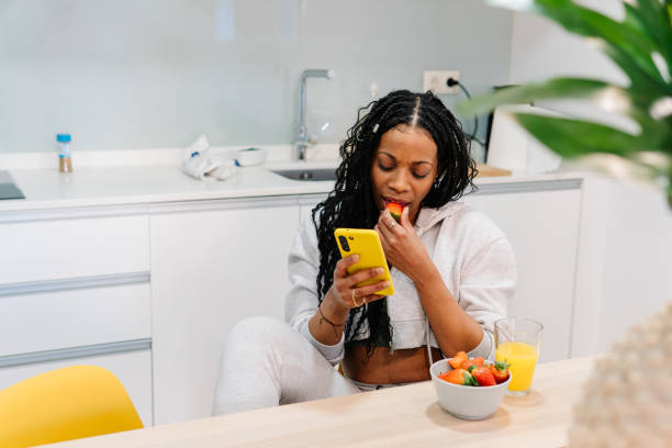 istock Young woman eating strawberries, drinking orange juice at kitchen table, scrolling smartphone during morning meal 2196358653