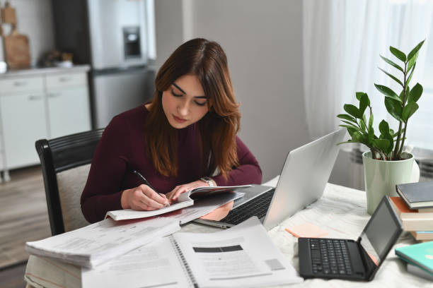 istock Studious Woman Writing Important Points in Planner While Laptop and Books Nearby 2196363219