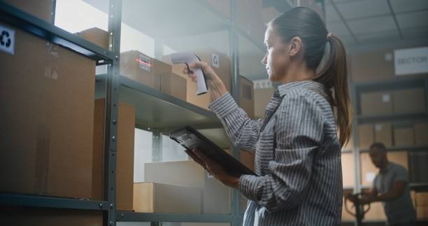 istock Female Warehouse Associate Scans Cardboard Box, Checks Information on Tablet Computer, 2196365351