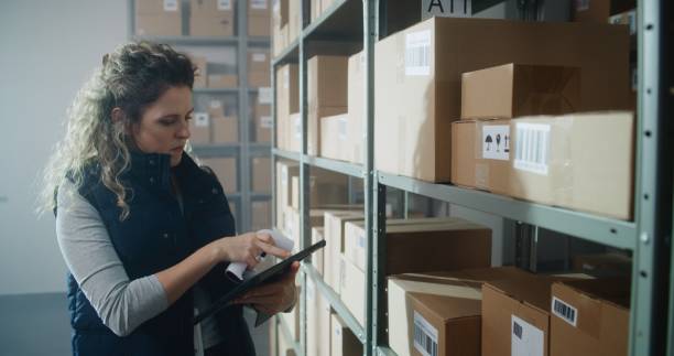 istock Female Warehouse Associate Scans Cardboard Box, Checks Inventory on Tablet Computer 2196366352