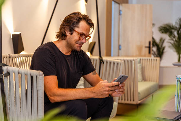 istock A man is sitting on a couch and looking at his cell phone 2196368693