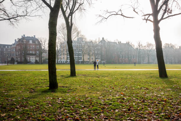 Amsterdam, Netherlands - Dec 1, 2019: Morning view across a public park. Pedestrians on a pavement. Winter atmospheric haze clouds the classic residential buildings in the background.