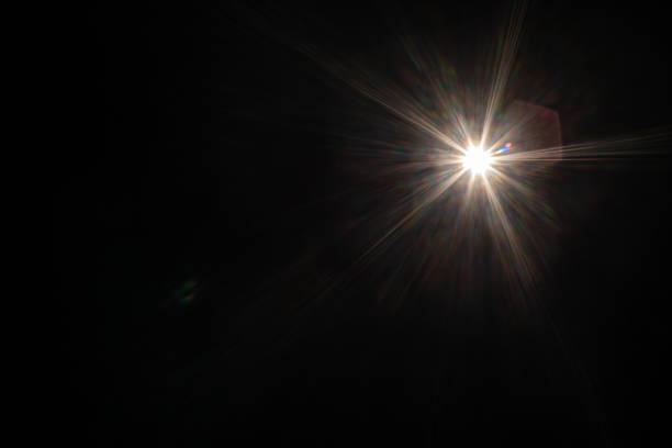 Bright light shines against dark background creating lens flare, starburst effect.