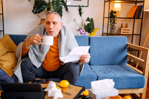 istock Middle age man sitting on sofa bed feeling sick at home and drinking hot tea while looking at prescription 2196384278