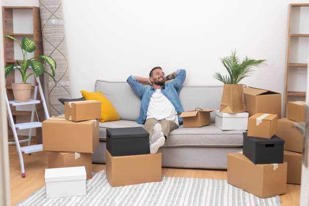 istock happy man with cardboard boxes in new home on moving day, relaxing on sofa relocation 2196388977