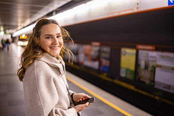 istock Smiling woman checking her phone while waiting subway train 2196390188
