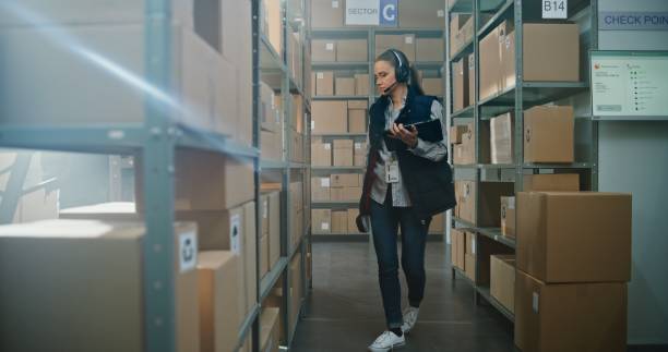 istock Female Inventory Manager Wearing Headset Scans Parcels in Warehouse Facility 2196391439