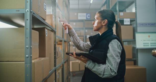 istock Female Inventory Specialist Scans Parcels in Warehouse Retail Facility, Uses Tablet Computer 2196392845