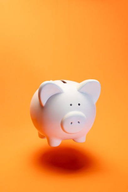 istock Ceramic white piggy bank positioned against bright orange backdrop, representing financial planning and saving concepts with clean, minimalist aesthetic 2196394418