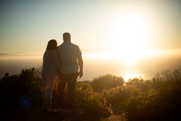 Couple, ocean and back with view, sunset and memory with mockup space, mountain and horizon in summer. Mature people, outdoor and interracial love by sea with partner, nature and bonding on vacation