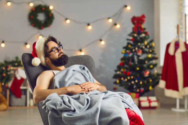 istock Bearded funny man in Santa cap sleeping in armchair under blanket 2196400461