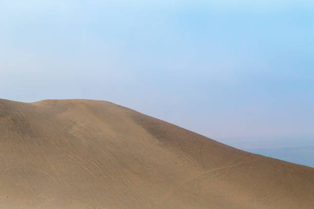 Vast sand dunes create a mesmerizing landscape under a hazy sky in huacachina, peru, a popular destination for adventure and exploration