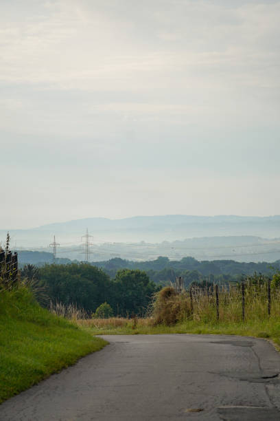 Rural view of asphalted road leading to hills around 200m over sea level with blue foggy background, North Rhine-Westphalia, Germany