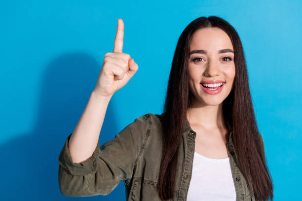 istock Young woman smiling and pointing upwards against a bright blue background 2196405423