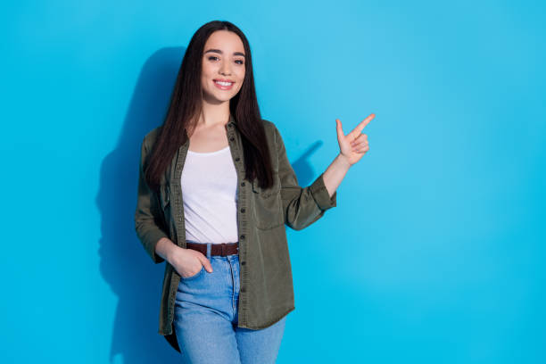 istock Young woman smiling and pointing to the side on a blue background 2196405536