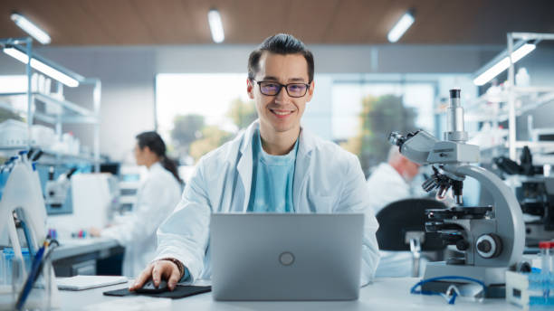 istock Portrait of a Handsome Young Multiethnic Lab Engineer in White Coat Looking at Camera and Smiling. Genetic Research Scientist Working on a Laptop Computer in an Applied Science Laboratory 2196408684