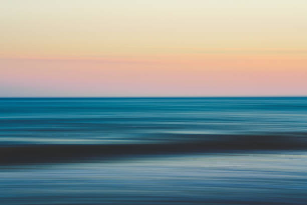 istock Blurred ocean waves stretch toward a pastel sunset sky. 2196409192