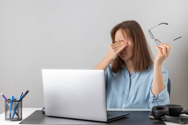 istock A stressed female freelancer at a desk, rubbing her eyes while working on a laptop. She wears glasses, appears exhausted, and struggles with eye strain, burnout, and tension 2196411037