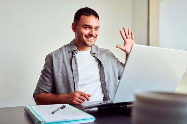 Smiling freelancer waving hand during video conference at home office