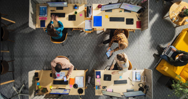 istock Top Down View: Diverse Team of Professionals Working on Digital Projects in an Office. Businesspeople Analyze Data and Use Laptops. Creative Workspace with Charts, Infographics, and Discussions. 2196418314