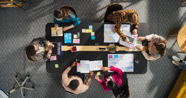 istock Top Down View: Diverse and Creative Colleagues Working Together at The Conference Table In Stylish Office. Male and Female Business People Using Tablets, and Laptops to Analyze Business Data on Charts 2196418458