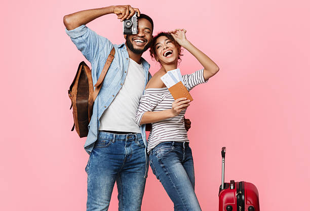 Ready for vacation. Happy couple with suitcase and tickets over pink background
