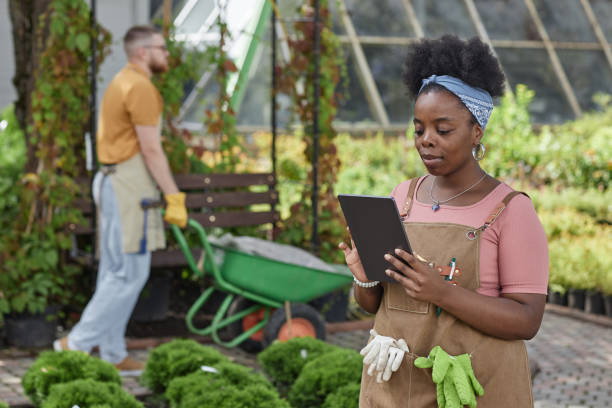 istock Black Female Horticulturalist Using Tablet Computer Inspecting Plants in Garden Center 2196422217