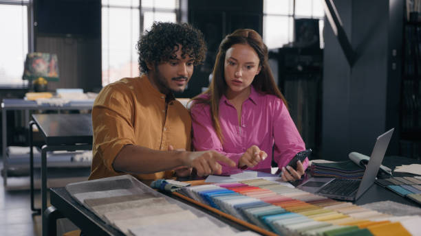 istock Multiracial couple creative designers work in modern office studio Arabian Indian man Caucasian woman using phone choosing perfect sample of material color tone for new house interior design project 2196422417