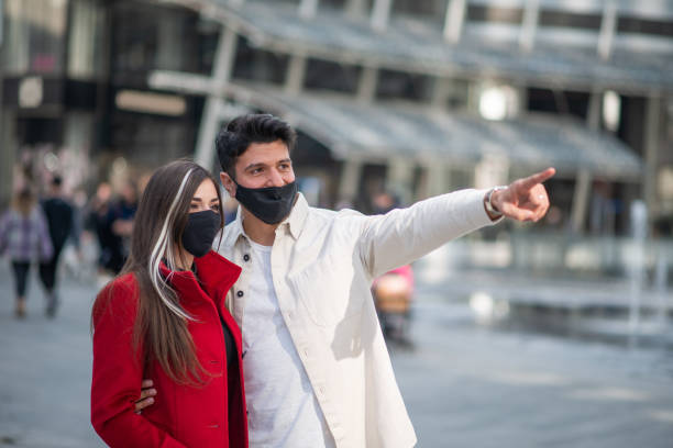 istock Young couple wearing protective face masks pointing at something while walking in the city center 2196429657