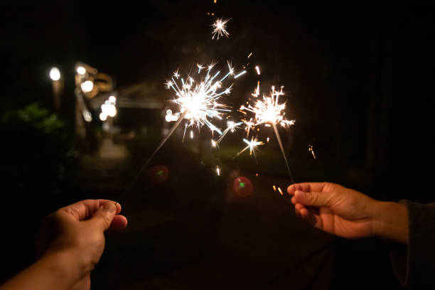 istock Two hands hold sparklers, illuminating the dark night with sparkling light 2196430404