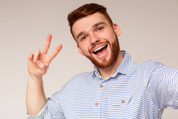 istock Young millenial man showing V - sign and making selfie 2196431582