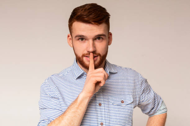 istock Young man showing silence sign and putting finger to lips 2196431626