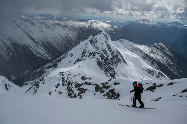 Backcountry skier climbs mountain above valley and ranges, Tantalus Ranges