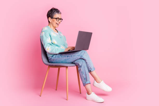 istock Elderly woman smiling and working on laptop against a pink backdrop 2196440081